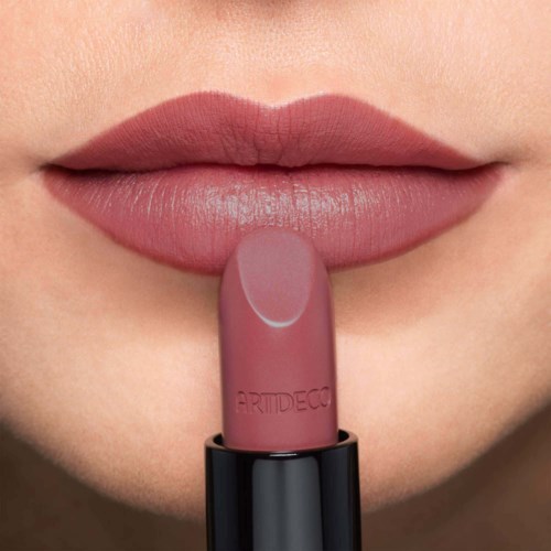 Nahaufnahme von Lippen mit hellrosa Lippenstift und einem passenden Lippenstiftstift in der Nähe der Lippen.