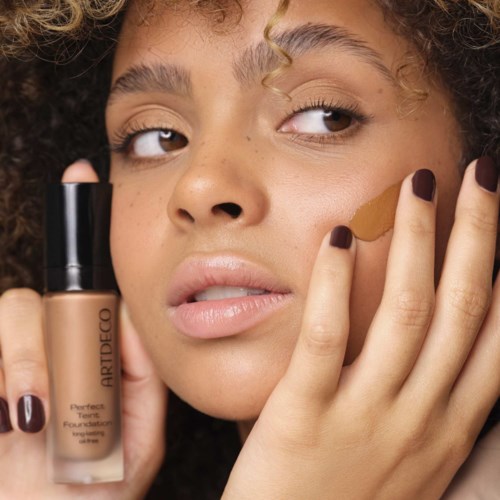 Een vrouw brengt foundation aan op haar gezicht, houdt een make-up fles vast en gebruikt haar vingers om te blenden.