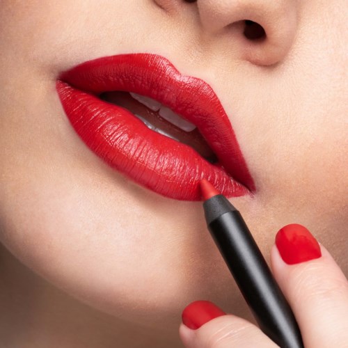 Eine Frau trägt leuchtend roten Lippenstift auf die Lippen auf, mit ihrem Finger, der den Lippenstiftstift an der Unterlippe hält.