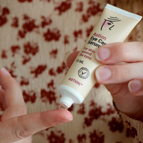 A person applying eye care serum around their eyes from a small tube.