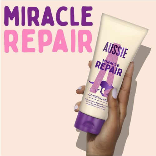 A hand holds a purple and white bottle labeled 'Aussie Miracle Repair' conditioner with large text above.