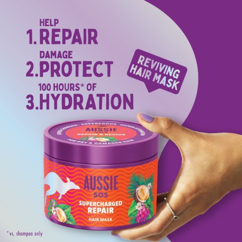 A hand holding a purple and orange hair mask container with text about repairing and protecting hair, promoting hydration.