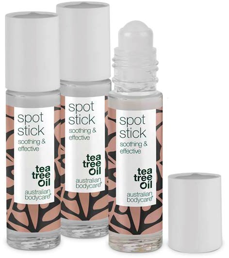 Drie flessen tea tree olie spot stick met witte doppen en labels, met zwart en perzik ontwerp. Eén dop verwijderd.