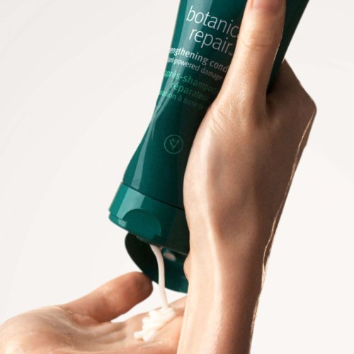 Eine Person drückt Creme aus einer grünen Flasche mit der Aufschrift botanic repair. Die Creme fällt in ihre Hand.