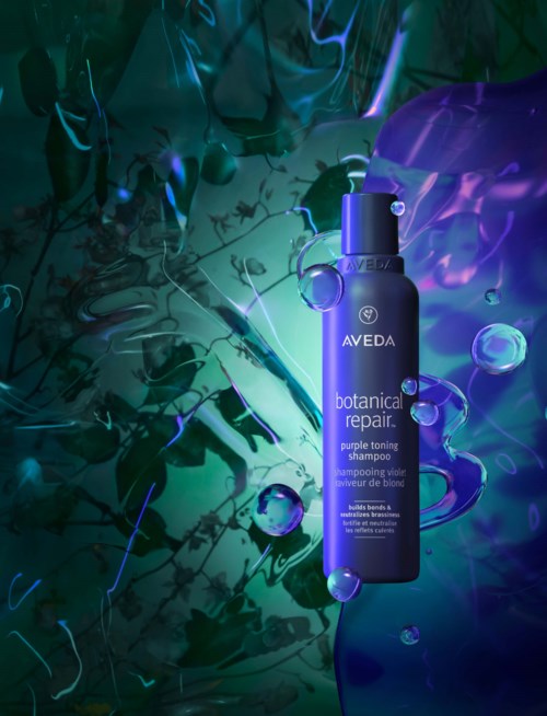 Eine blaue Flasche des Aveda Botanical Repair Shampoos umgeben von blauen und lila abstrakten Formen und Blasen.