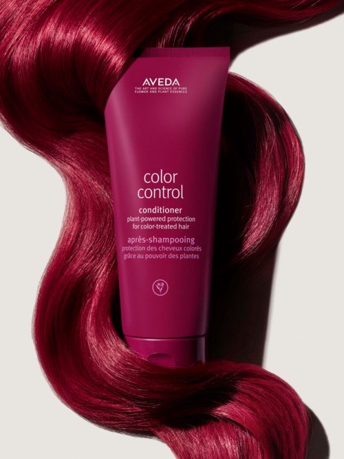 En rosa flaska med Aveda balsam omgiven av långa, glänsande, röda hårstrån.