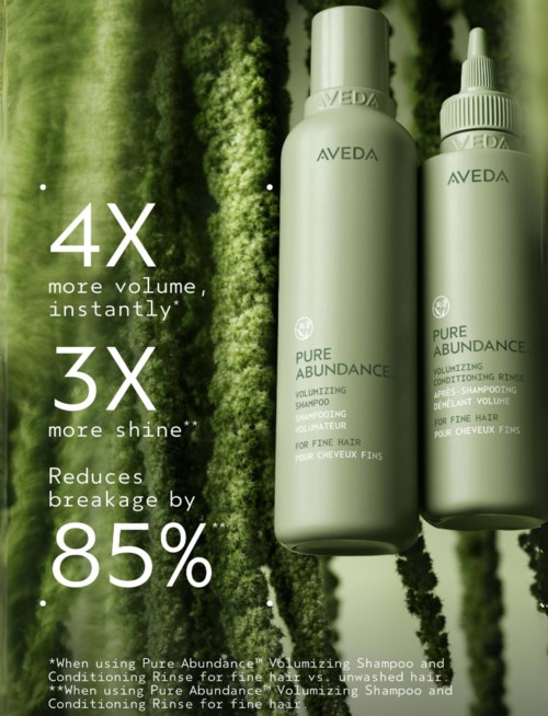 Zwei weiße Flaschen mit Aveda Pure Abundance Haarprodukten vor grünem Hintergrund. Text hebt Volumen, Glanz und geringere Haarbrüche hervor.