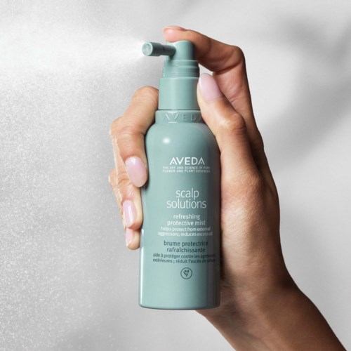 Eine Hand hält eine hellgrüne Flasche mit Aveda scalp solutions gegen einen schlichten Hintergrund.