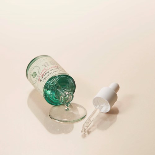 Een fles vloeistof, pipet en een klein glazen schaaltje op een eenvoudige ondergrond.