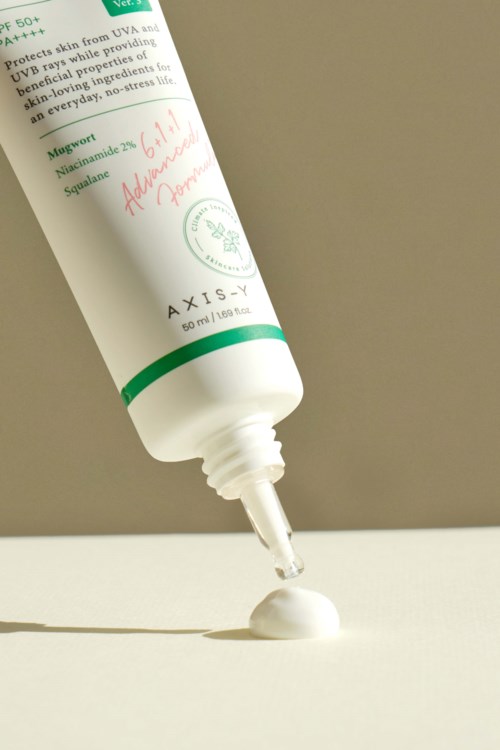 Een witte huidverzorgingsfles met groene en rode tekst, die crème op een witte ondergrond aanbrengt.