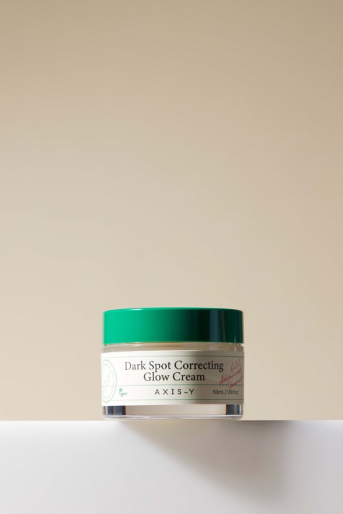 Een potje met dark spot correcting glow cream met groen deksel op een witte ondergrond.