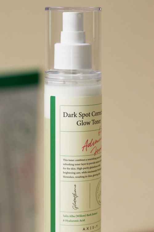 Een witte pompflacon met label voor donkere vlekken en glow, met groene en rode tekst, tegen een lichte achtergrond.