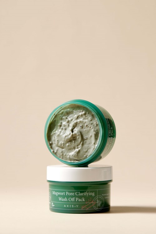 Een kleine groene pot met deksel, met een romige huidverzorgingsproduct, labeled "Magwort Pore Clarifying Wash Off Pack."