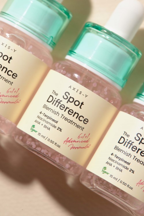 Drie flessen van vlekkenbehandeling met roze vloeistof en groene doppen, gemerkt 'The Spot Difference' door Axisy.