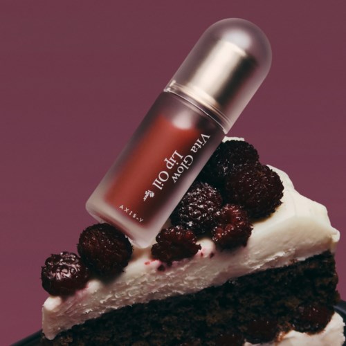 Een lipstick ligt op een stuk taart met bessen erop, tegen een paarse achtergrond.