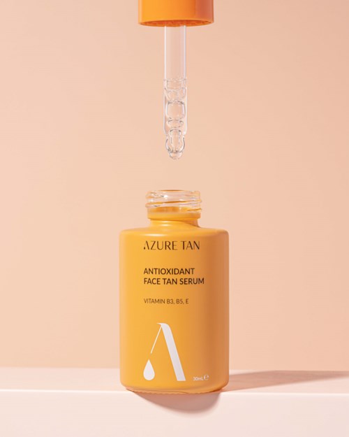 Eine gelbe Flasche mit dem Label Azure Tan Antioxidant Face Tan Serum und einer Pipette darüber. Die Pipette gibt Serum ab.
