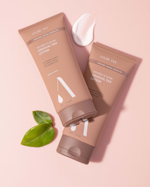 Zwei beige Tuben Lotion liegen auf rosa Hintergrund, mit einem grünen Blatt und einem Klecks Creme.