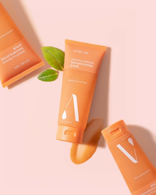 Drei orange Hautpflege-Tuben mit weißen Texten und einem kleinen grünen Blatt auf einem rosa Hintergrund.