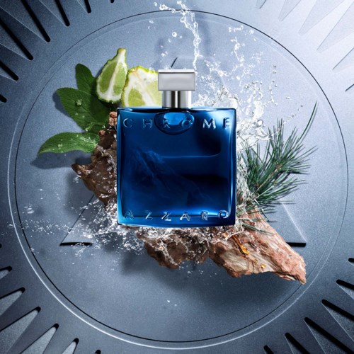 Een blauwe parfumfles met 'Chrome' op een rots, met limoenpartjes, dennentak en waterspetters eromheen.