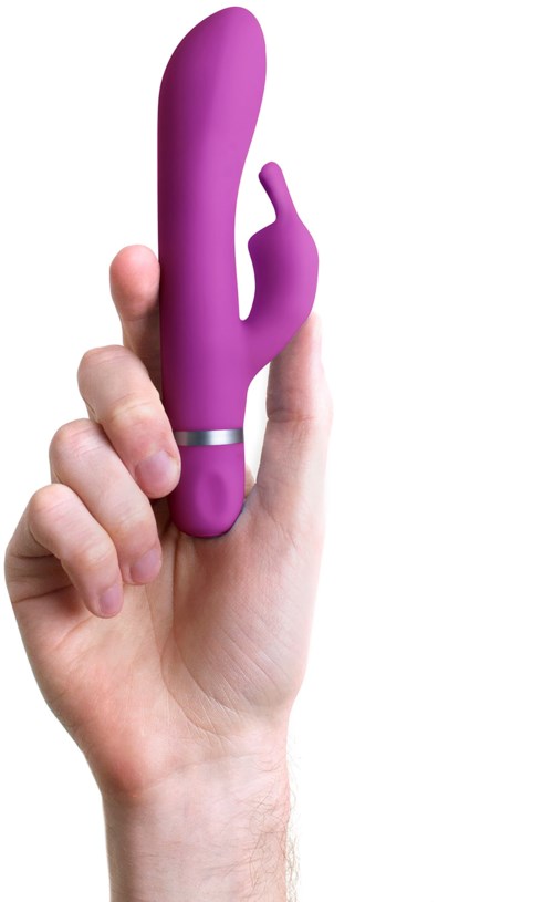 Eine Hand hält einen lila, gekrümmten Erwachsenen-Spielzeugroboter mit einem kleinen Finger. Der Hintergrund ist weiß.