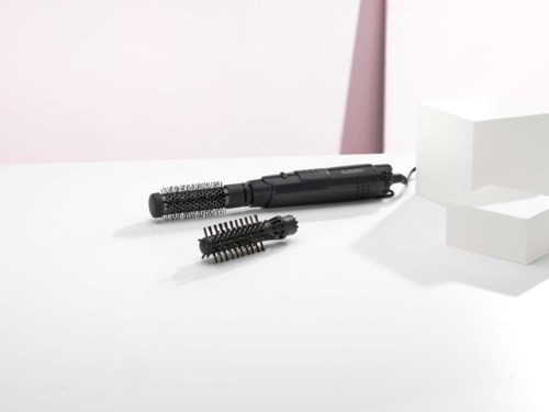 A black heated styling device with two different brush attachments on a white surface.