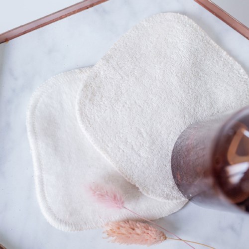 Cotton pads and a brown bottle on a light background. A cotton pad is in front, with some pink fiber nearby.