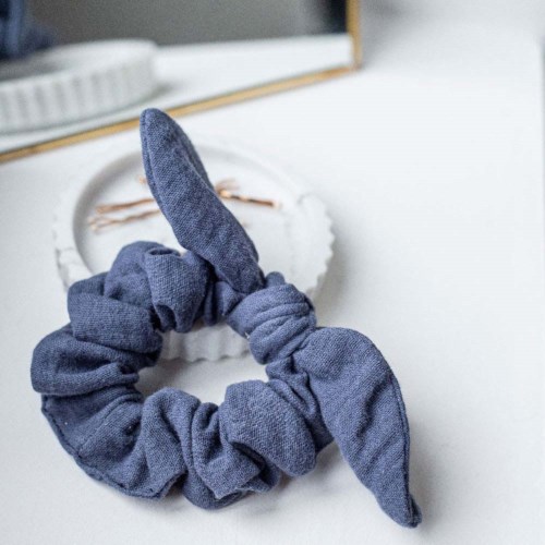 A blue scrunchie with a tied bow is placed on a white surface near a mirror.