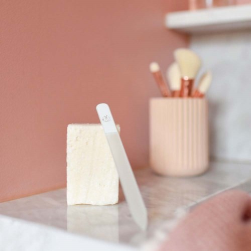 A soap bar and a razor stand on a counter with a pink wall and a container of makeup brushes in the background.