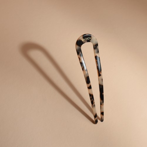 A leopard print hair clip stands on a beige surface, casting a shadow to the left.