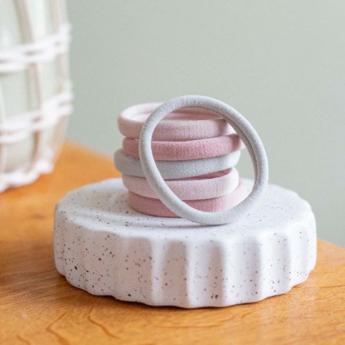 A stack of pink and grey hairbands on a white stone surface, with a plain background.