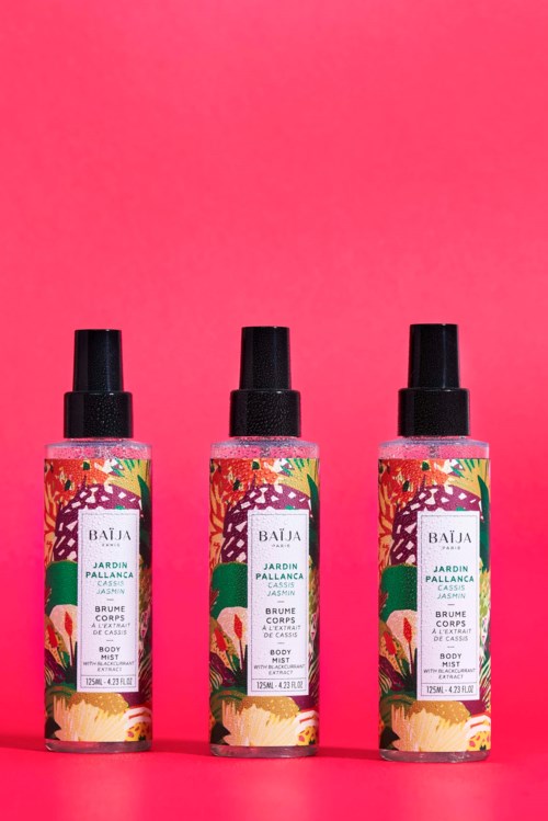 Three body spray bottles with colorful floral labels stand on a pink background.