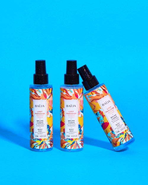 Three body spray bottles with bright, colorful labels and black caps against a blue background.
