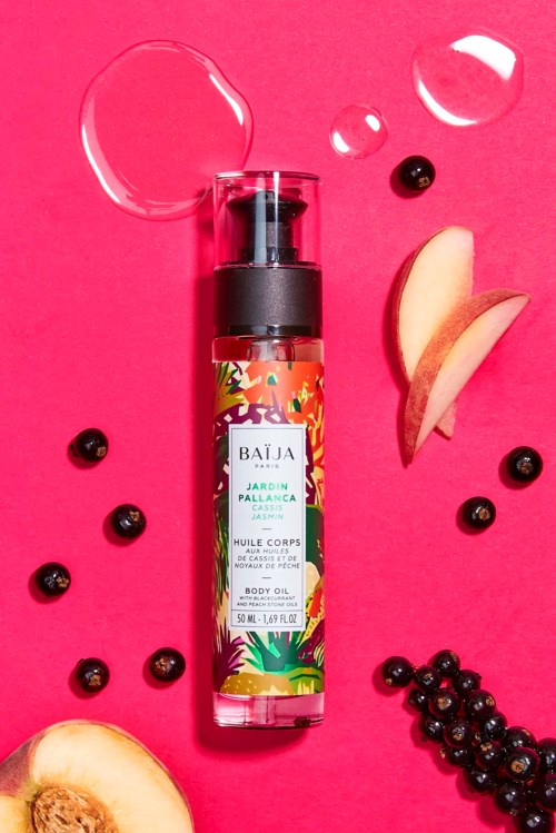 A body oil bottle surrounded by apple slices, blackberries, and bubbles on a pink background.