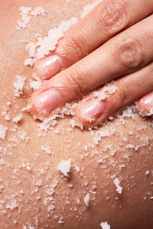A hand pressing salt crystals onto skin, showing salt granules on flesh.