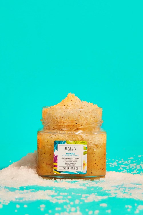 A jar of exfoliating salt scrub labeled 'Baía,' with salt spilled around it on a blue background.