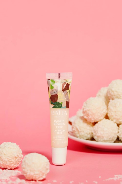 A tube of beauty cream is placed on a pink background with white fluffy balls nearby.