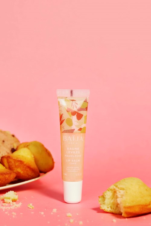A tube of lip balm stands among cookies on a pink background.