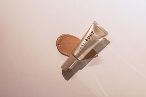 Een tube met 'BALIBODY' erop met bruine crème ernaast op een witte ondergrond.