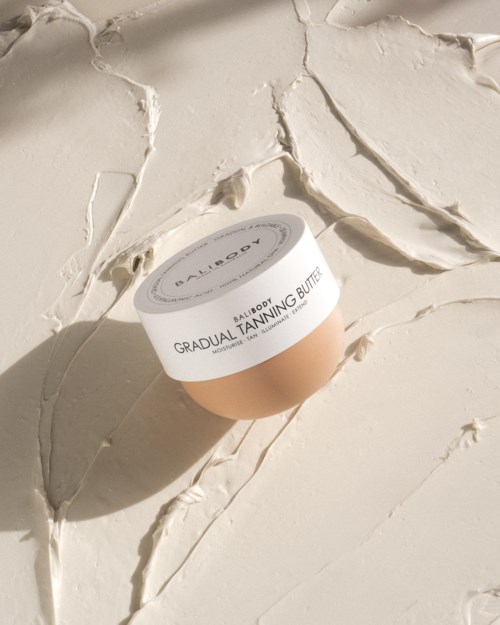 Een cosmeticaverpakking met 'Gradual Tanning Butter' ligt op een gestructureerd, crèmekleurig oppervlak.