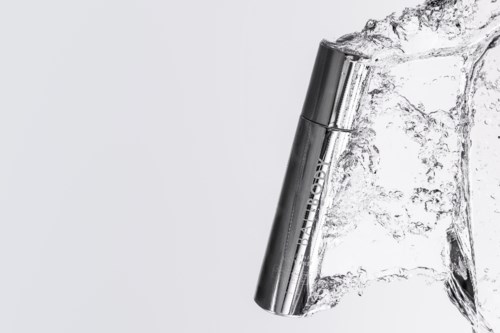Een zilveren cilindervormig apparaat dat met water spettert, met metalen afwerking, tegen een eenvoudige achtergrond.
