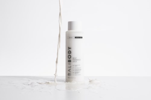 Een witte fles met 'BODY' erop, staat op een witte oppervlakte met vloeistof die van boven stroomt.