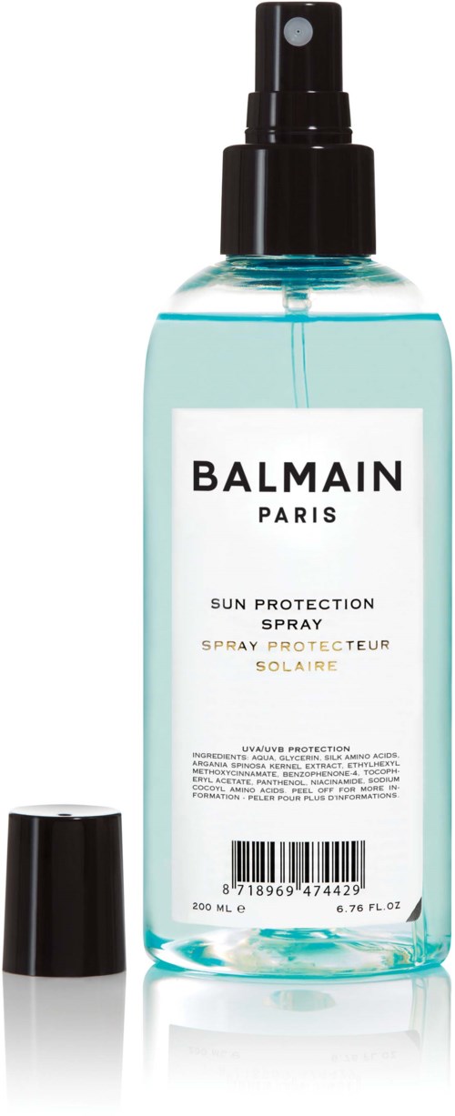En klar sprayflaska märkt Balmain Paris solskyddsspray, med en svartmunstycke och lock.