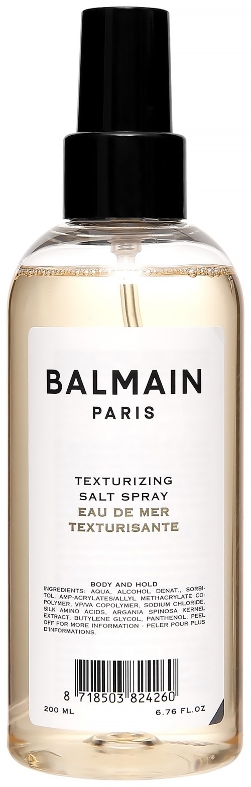 Een doorzichtige sprayfles met een zwarte dop en wit label, met merknaam Balmain Paris Texturizing Salt Spray, 200 ml.
