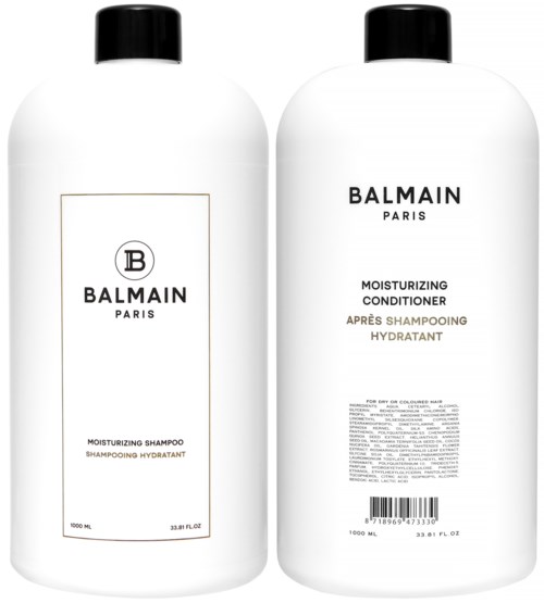 Kaksi valkoista pulloa mustilla lukkoilla, merkitty Balmain Paris, shampoolle ja hoitoaineelle. Yksinkertainen muotoilu, 1000 ml kummallekin.