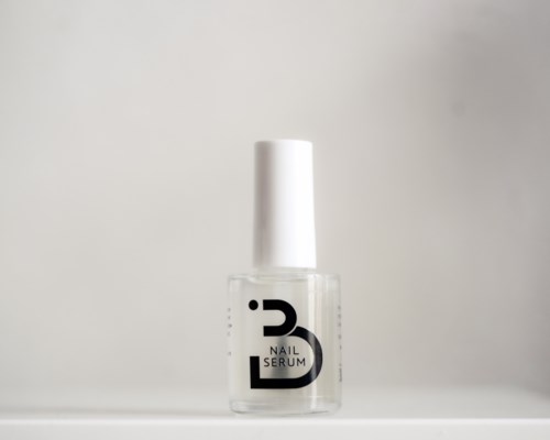 A clear nail serum bottle with a white cap, standing on a plain surface against a neutral background.