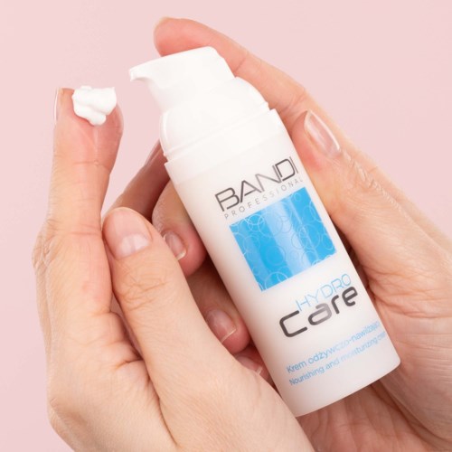 A person applies a white cream from a bottle labeled 'BAND Professional Hydro Care' onto their finger.