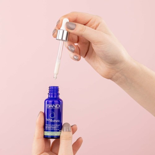A hand holds a dropper with a liquid and is about to apply it from a small blue bottle.