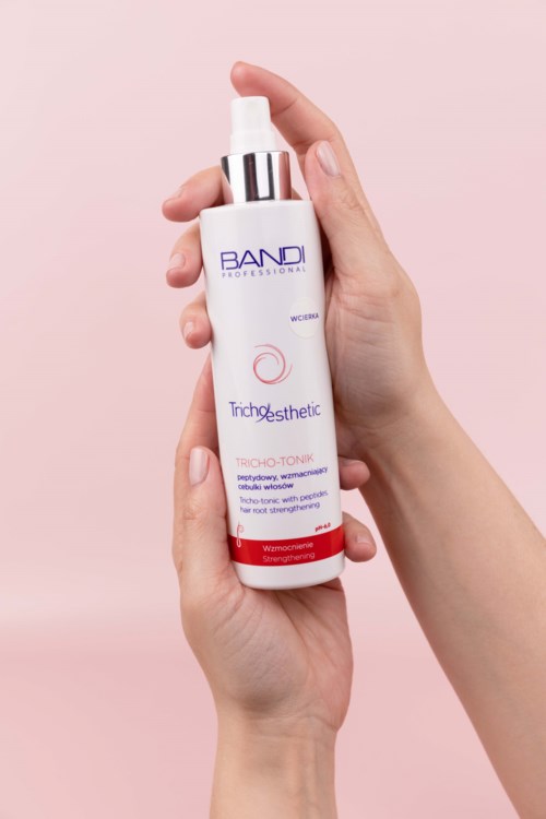 A person holds a white bottle with a spray top against a light pink background.