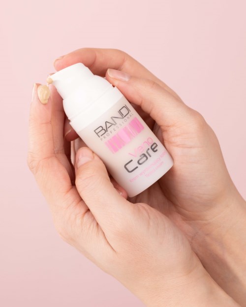 A hand holds a white bottle of skin care product with pink and black text on a light pink background.
