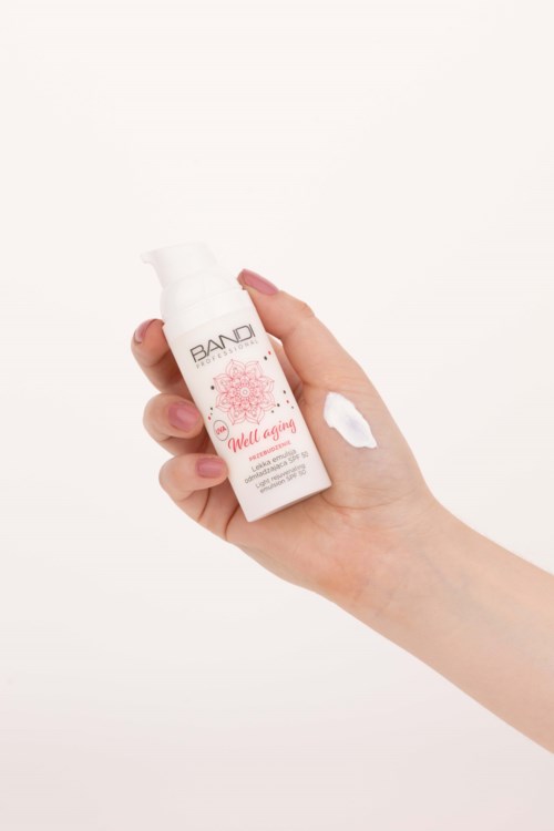 A hand holds a white bottle with pink designs and text, showing some white cream on the hand.